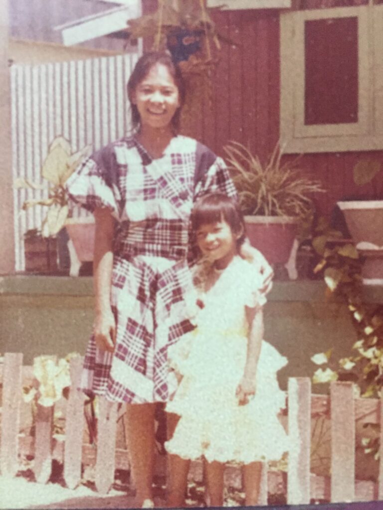 Vintage Christmas photograph of two Indonesian sisters in elegant plaid and white dresses standing in front of traditional home