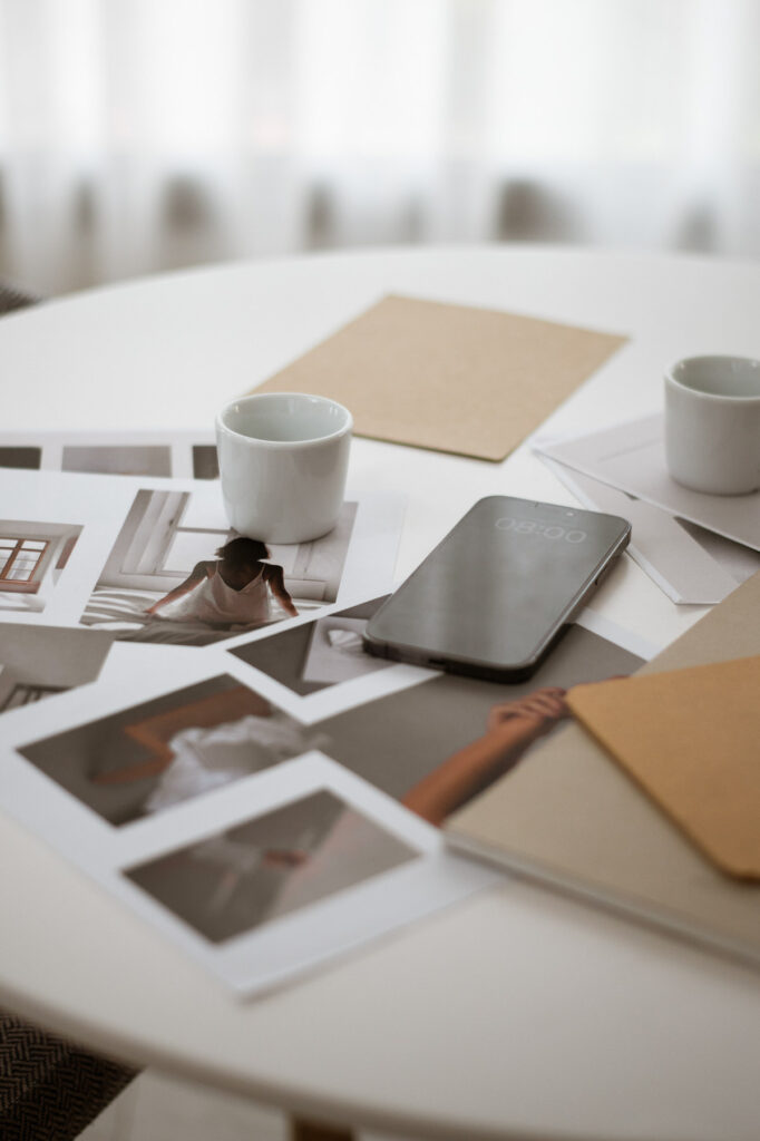 Minimalist white desk workspace with coffee cup, smartphone, and scattered photographs in soft natural lighting